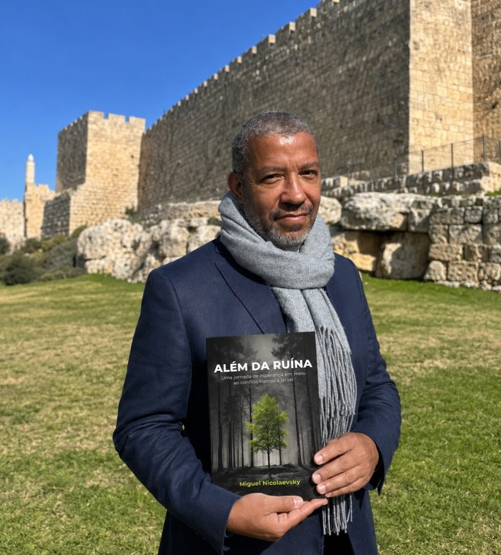 Miguel Nicolaevsky segurando o livro Al&eacute;m da Ru&iacute;na em frente as muralhas de Jerusal&eacute;m